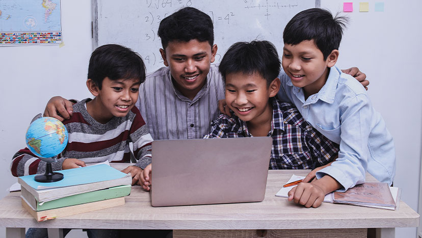 Guru menjelaskan pelajaran menggunakan laptop kepada siswa di kelas.